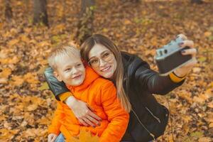 Son and mother are taking selfie on camera in autumn park. Single parent, leisure and fall season concept. photo