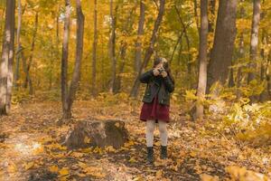 un pequeño niña tomar un foto con antiguo retro cámara en otoño naturaleza. ocio y pasatiempo concepto.