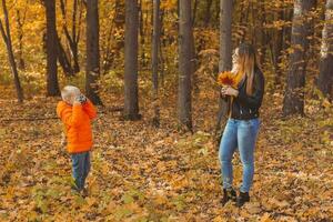 Boy photographer takes pictures of a mother in the park in autumn. Hobbies, photo art and leisure concept.