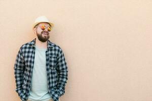 Bearded man in summer clothes and hat stand over beige wall on street city urban and travel concept - copy space and empty space for advertising photo