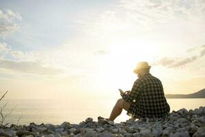 Rear side view of man with smartphone sitting on beach terrace on sunny day outside background with copy space - vacation or freelance or social network concept photo