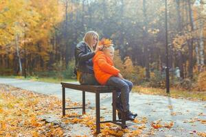 Single parent mother and child boy in the autumn in park sit on bench. Fall season and family concept. photo