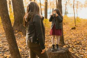 Child taking picture her mother on retro camera in autumn park. Hobbies and leisure concept. photo