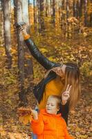 hijo y madre son tomando selfie en cámara en otoño parque. soltero padre, ocio y otoño temporada concepto. foto