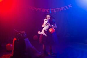 Funny child girl in witch costume for Halloween with pumpkin Jack and dog. photo