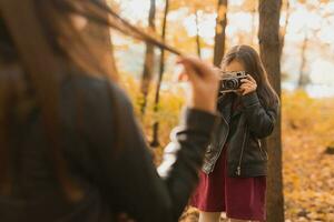 Child taking picture her mother on retro camera in autumn park. Hobbies and leisure concept. photo