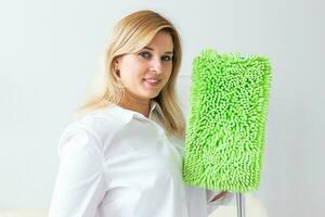 Smiling millennial woman housewife with mop for washes floor enjoys cleaning in minimalist interior. Household cleaning services and domestic work housekeeping photo