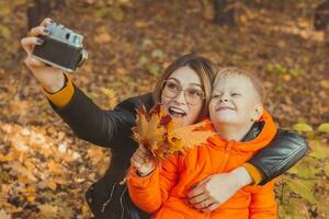 hijo y madre son tomando selfie en cámara en otoño parque. soltero padre, ocio y otoño temporada concepto. foto