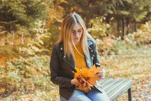 Cute smiley woman holding autumn leaves in fall park. Seasonal, lifestyle and leisure concept. photo