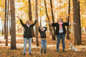 Grandmother and mother with granddaughter throw up fall leaves in autumn park and having fun. Generation, leisure and family concept. photo