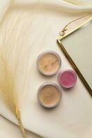 Cosmetics facial powder and blush for cheeks on natural background with dried flowers. Makeup accessories top view photo