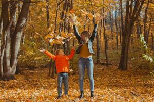 Single parent family playing with autumn leaves in park. Happy mom and son throw autumn leaves up in fall park. photo