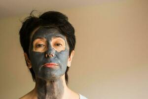 Cosmetology, spa, skin care and people concept - Woman applying Facial clay Mask. Beauty Treatments. photo