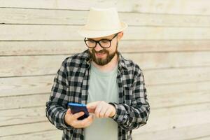 Smiling male tourist use smartphone during summer city break over wooden wall - technologies and social media app concept photo