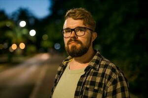 Portrait of man standing in night city street with bokeh street lights in background. Confident lonely guy. Close-up portrait photo