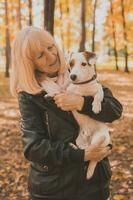 Senior smiling woman hugging her dog in autumn park. Active aging and pet concept. photo