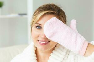 Excited joyful young woman wrapped head in towel holding dry brush shower sponge and doing spa procedure photo