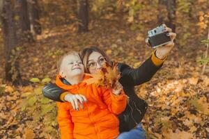 hijo y madre son tomando selfie en cámara en otoño parque. soltero padre, ocio y otoño temporada concepto. foto