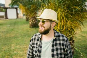 Laughing attractive man wearing hat over palm tree background with copy space - emotion and vacation travel holidays concept photo