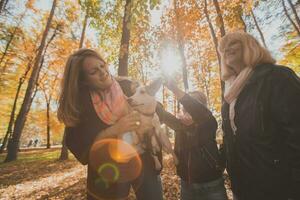 Mother and grandmother and daughter holds jack russell terrier and plays with it in autumn outside. Pet and family concept photo