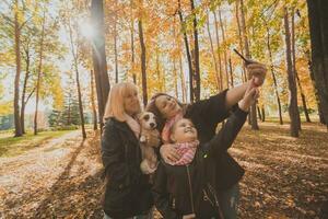 Mother, grandmother and little granddaughter with jack russell terrier dog taking selfie by smartphone outdoors in autumn nature. Family, pets and generation concept photo