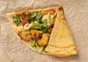 Pancake or crepe with fried shrimp tomatoes and vegetables and cheese top view photo