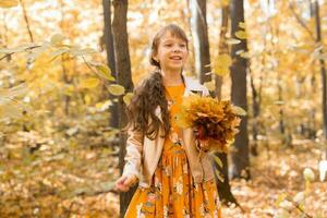 Little kid girl with autumn orange leaves in a park. Lifestyle, fall season and children concept. photo