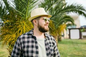 Laughing attractive man wearing hat over palm tree background with copy space - emotion and vacation travel holidays concept photo