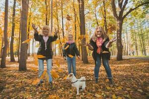 Grandmother and mother with granddaughter throw up fall leaves in autumn park and having fun. Generation, leisure and family concept. photo