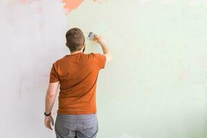 Man smoothes wall surface with a wall grinder. Male grind a white plaster wall - renovation and redecoration concept. Copy space and empty space for text photo