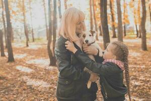 Grandmother with granddaughter in autumn park, girl hugging grandmother and her jack russell terrier dog. Generations, pet and family concept. photo