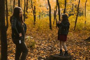 Child girl photographer takes pictures of a mother in the park in autumn. Hobbies, photo art and leisure concept.