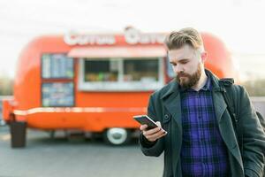 Portrait of handsome young man with smartphone standing in front of food truck photo