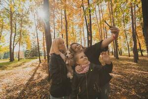 Mother, grandmother and little granddaughter with jack russell terrier dog taking selfie by smartphone outdoors in autumn nature. Family, pets and generation concept photo