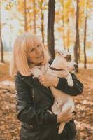 Senior smiling woman hugging her dog in autumn park. Active aging and pet concept. photo