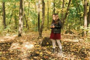 niño niña utilizando un Anticuado cámara en otoño naturaleza. fotógrafo, otoño temporada y ocio concepto. foto