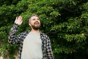 lado ver de Encantado masculino en pie al aire libre y ondulación mano a su amigo. él es alegre a reunirse su familiarizado por oportunidad. Copiar espacio y sitio para publicidad foto