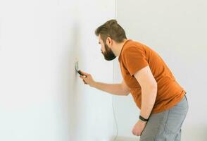 Man smoothes wall surface with a wall grinder. Male grind a white plaster wall - renovation and redecoration concept photo