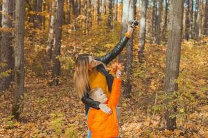 hijo y madre son tomando selfie en cámara en otoño parque. soltero padre, ocio y otoño temporada concepto. foto
