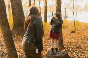 Child girl photographer takes pictures of a mother in the park in autumn. Hobbies, photo art and leisure concept.