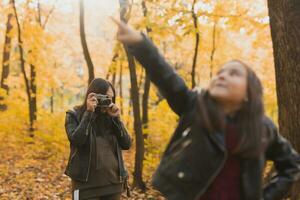 Mother photographer takes pictures of a her daughter in the park in autumn. Hobbies, photo art and leisure concept.