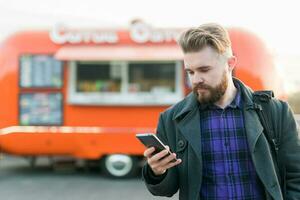 Portrait of handsome young man with smartphone standing in front of food truck photo