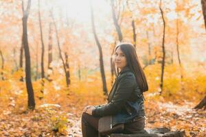 Young woman sits alone on wooden stump while walking through forest on an autumn day. Loneliness and melancholy concept. photo