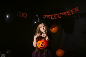 Funny child girl in witch costume for Halloween with pumpkin Jack. photo