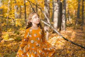 pequeño niño niña con otoño naranja hojas en un parque. estilo de vida, otoño temporada y niños concepto. foto