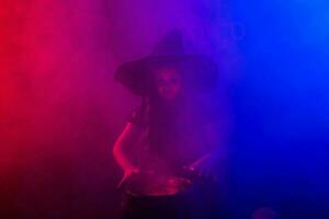 Child girl witch preparing a potion in the cauldron at halloween holidays. Copy space. photo