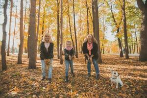 Grandmother and mother with granddaughter throw up fall leaves in autumn park and having fun. Generation, leisure and family concept. photo