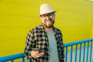 Bearded hipster guy in glasses using smartphone technology for making online booking and banking during travel vacations - millennial blogger with beard messaging in social networks in street photo