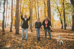 Grandmother and mother with granddaughter throw up fall leaves in autumn park and having fun. Generation, leisure and family concept. photo