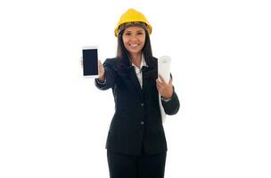 portrait of asian engineer woman with helmet holding blueprints and showing blank screen mobile phone isolated white background photo